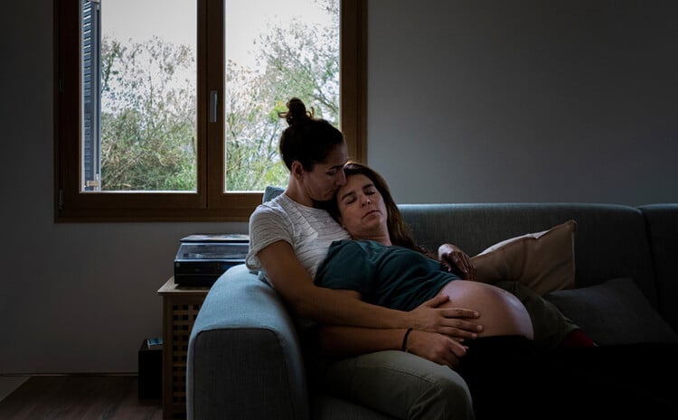 Two pregnant women are sitting in each other's arms