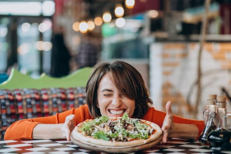 молодая красивая женщина ест пиццу в пиццерии Διατροφη